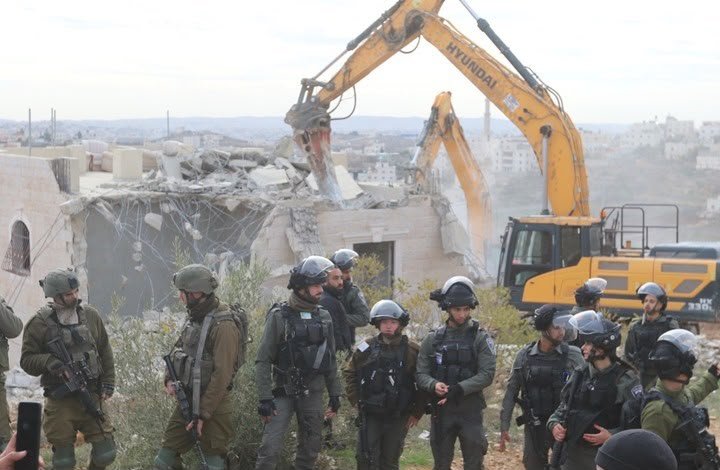 Armed forces standing while a house is demolished in the West Bank